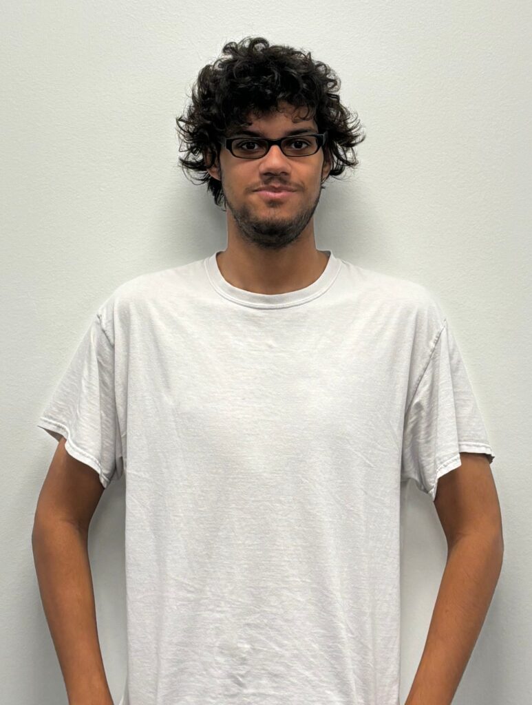 Appliance Repair Parts Facilitator from Richland Hills wearing glasses and a plain white t-shirt, standing against a light-colored wall, supporting Guinco’s efficient parts operations.
